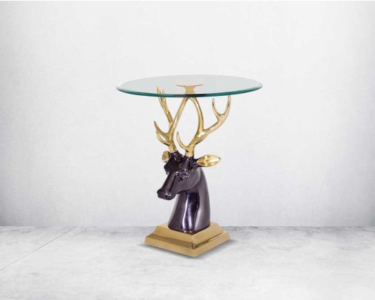 A sculptural end table made of solid aluminium in gold finish with a tempered clear glass top & reindeer design base
